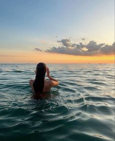 a woman sitting on top of a surfboard in the middle of the ocean at sunset