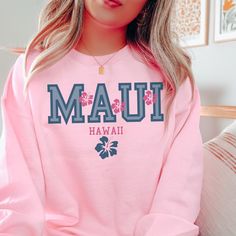 a woman wearing a pink sweatshirt with the word mau hawaii printed in blue on it