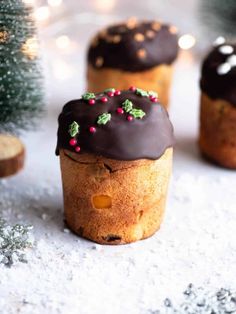 three muffins with chocolate frosting and sprinkles on them sitting next to a christmas tree