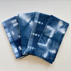 four blue napkins with white designs on them sitting next to each other in front of a white background