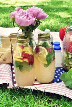 two mason jars filled with lemons, strawberries and limeade on a picnic blanket