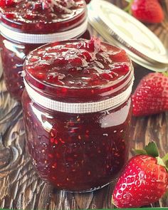 three jars filled with jam sitting on top of a wooden table next to strawberries