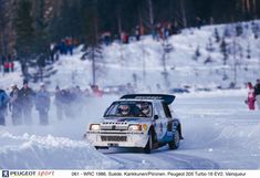 a rally car driving down a snow covered road with people watching from the sidelines