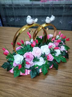 two wedding rings with pink and white flowers in them sitting on a wooden table next to a window