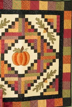 a quilted wall hanging with an orange pumpkin on it's center and leaves