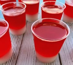 several glasses filled with red liquid sitting on top of a wooden table