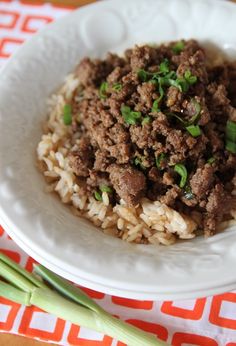 a white plate topped with meat and rice on top of a red and white table cloth