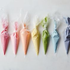 six different colored candy cones wrapped in cellophane on a white surface, lined up and ready to be eaten