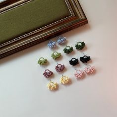 there are several pairs of small earrings on the table next to a framed picture and some beads