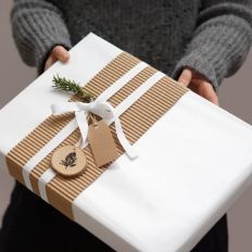 a person holding a wrapped present box with a white ribbon and brown tag on it