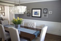 a dinning room table with white chairs and pictures on the wall behind it,