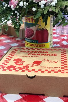 a box with some flowers in it sitting on a checkered tablecloth covered table