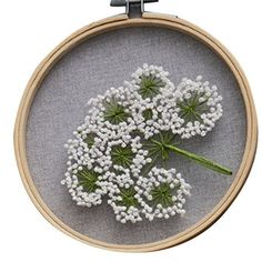 a close up of a cross stitch pattern with white flowers on a gray cloth background