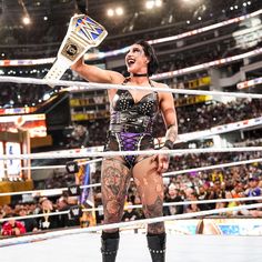 a female wrestler is holding her arm up in the air while standing on a wrestling ring