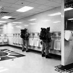 two men with backpacks standing next to urinals in a public washroom