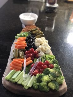 a wooden cutting board topped with lots of veggies and other foods on top of a black counter