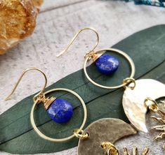 "Introducing: The \"Astraea\" collection PART 2. The Astraea features hammered metals, celestial elements and geometric shapes that form a gorgeous collection inspired by Greek goddess Astraea. Perfectly completed with deep blue lapis lazuli gemstone drops - Brass metal materials - 14k gold plated earring hooks - Gold plated brass Sun charms with tiny faux pearl inlay - Rubber ear nut backers included - 10mm lapis lazuli gemstone 2021©Wanderlust Hearts designs All Rights Reserved. WanderlustHear Bohemian Lapis Lazuli Earrings, Artisan Gold Lapis Lazuli Jewelry, Artisan Gold Jewelry With Lapis Lazuli, Celestial Style Wire Wrapped Brass Jewelry, Celestial Brass Jewelry With Wire Wrapped Detail, Celestial Brass Wire Wrapped Jewelry, Gold Bohemian Jewelry With Lapis Lazuli, Bohemian Gold Lapis Lazuli Jewelry, Gold Bohemian Lapis Lazuli Jewelry