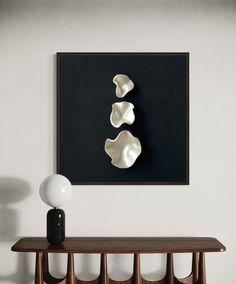 a table with two vases on it next to a black and white wall hanging