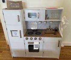 a play kitchen with white cabinets and wood floors in a room that has hard wood flooring