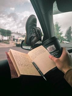 a person sitting in a car holding an open book and a coffee cup with writing on it