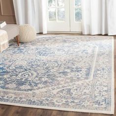 a large blue and beige rug in front of a window with white drapes on the windowsill