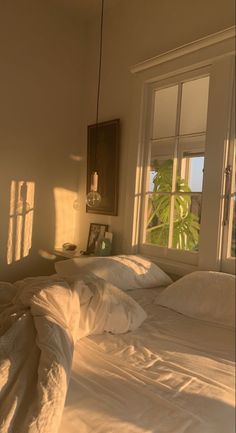 an unmade bed with white sheets and pillows in front of a window that looks out onto the ocean