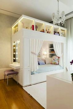 a white bed with curtains and lights on it in a room next to a window