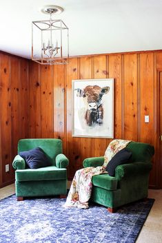 two green chairs in a room with wood paneling and a painting on the wall