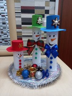 three snowmen made out of toilet paper sitting on a plate with decorations around them