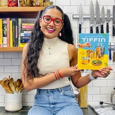 a woman sitting on a kitchen counter holding up a cookbook