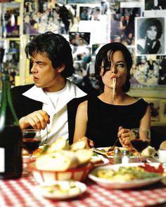 a man and woman sitting at a table with food in front of them, drinking wine