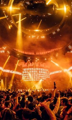 a large group of people at a concert with their hands in the air and lights on