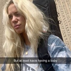 a woman with long blonde hair standing next to a suitcase