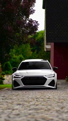 a white car parked in front of a red house on a cobblestone road