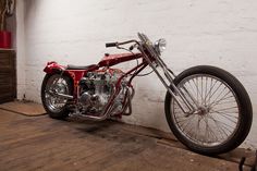 a red and black motorcycle parked next to a white brick wall in a room with wood flooring