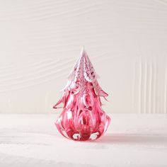 a pink glass vase sitting on top of a white table next to a wooden wall