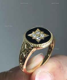 a gold ring with black onyx and white diamonds in the center, held up by someone's hand