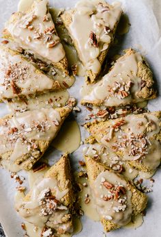 a plate topped with scones covered in icing and pecans on top of parchment paper