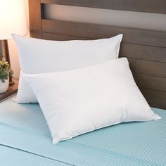 two white pillows sitting on top of a bed next to a night stand with a lamp