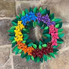 a multicolored wreath with leaves and flowers on it sitting against a stone wall