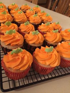 cupcakes with orange frosting and green leaves on top sit on a cooling rack