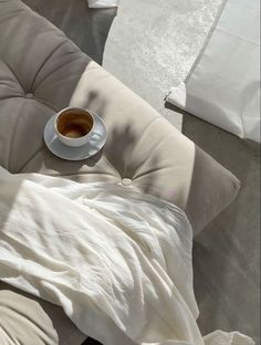 a cup of coffee sitting on top of a white couch next to pillows and blankets