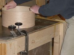 a man working on a wooden object with two hands and a vise in the background