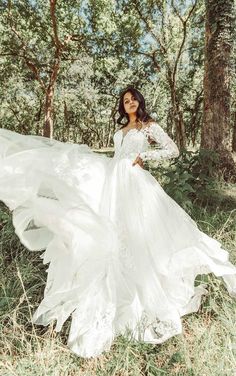 a woman in a white dress is standing in the woods with her hands on her hips