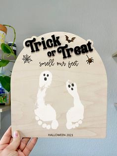 a person holding up a wooden sign that says trick or treat smell our feet on halloween