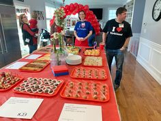 two people standing at a table with many trays of food on it and balloons in the background