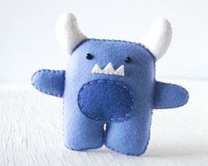 a blue stuffed animal with white horns on it's head and eyes, sitting on a white surface