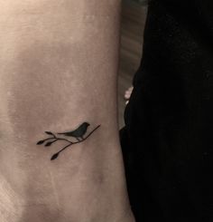 a small bird on a branch tattoo on the left arm and wrist is shown in black ink