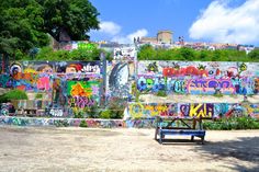 people are standing in front of a wall covered with colorful graffiti and trees on a sunny day