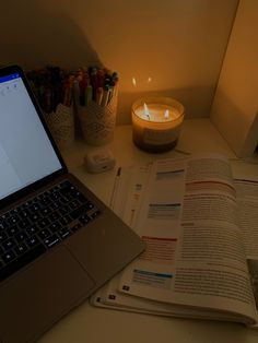 a laptop computer sitting on top of a desk next to an open book and candle